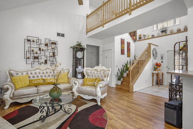 living area featuring wood finished floors, visible vents, baseboards, a high ceiling, and stairs