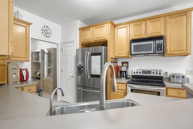 kitchen with light brown cabinetry, stainless steel appliances, light countertops, and a sink