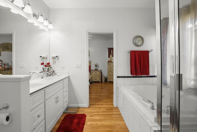 bathroom with double vanity, a bath, wood finished floors, and a sink