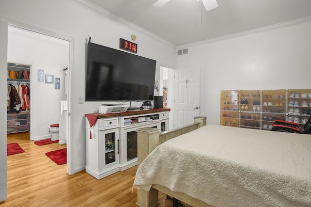 bedroom with wood finished floors, visible vents, baseboards, a spacious closet, and crown molding