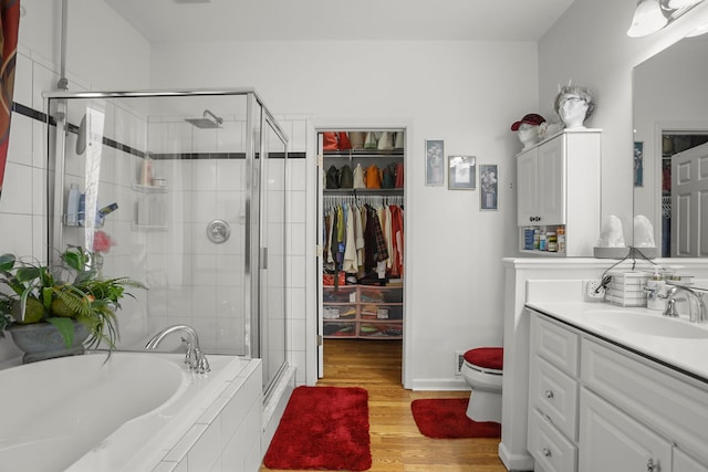 bathroom with a garden tub, toilet, wood finished floors, a shower stall, and vanity