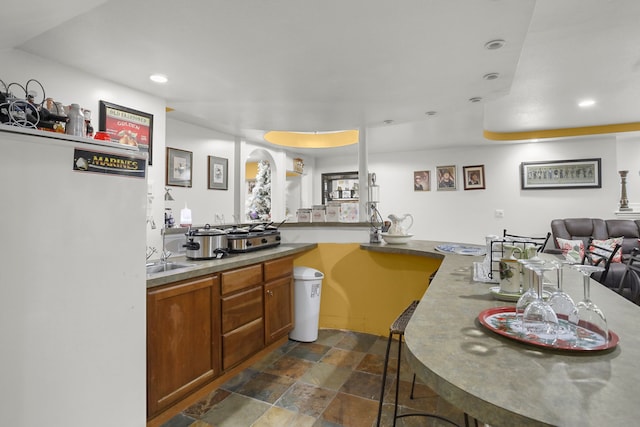 kitchen featuring open floor plan, recessed lighting, brown cabinetry, stone finish floor, and fridge