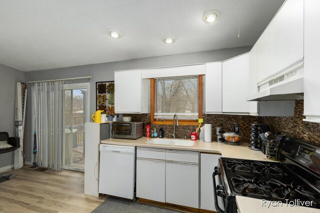 kitchen featuring white dishwasher, black gas range, under cabinet range hood, a sink, and white cabinetry