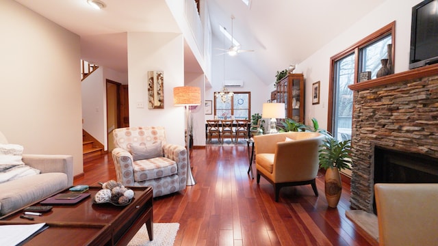 living area with a wall unit AC, dark wood finished floors, stairway, ceiling fan, and a stone fireplace