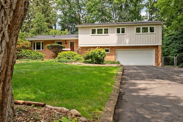 tri-level home featuring aphalt driveway, brick siding, an attached garage, fence, and a front lawn