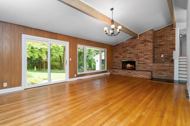 unfurnished living room featuring a notable chandelier, lofted ceiling with beams, a brick fireplace, wood finished floors, and stairs