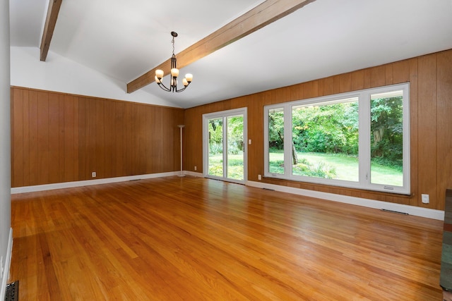 empty room with a chandelier, wooden walls, lofted ceiling with beams, and light wood-style floors