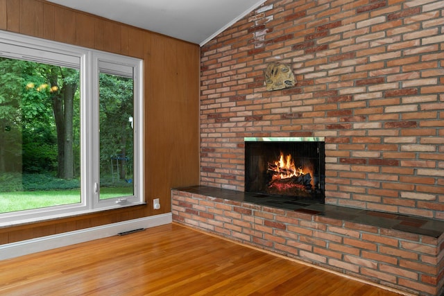 unfurnished living room with lofted ceiling, plenty of natural light, wood walls, and wood finished floors