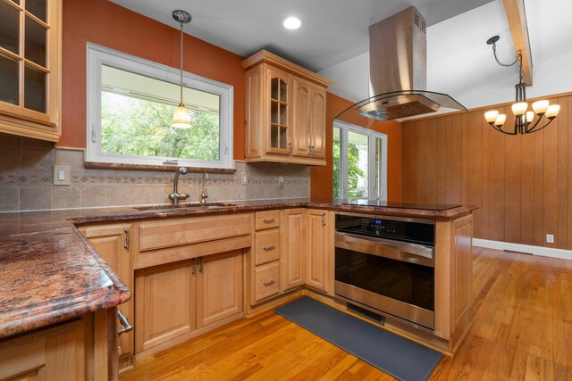 kitchen with black electric stovetop, oven, island range hood, a sink, and a wealth of natural light