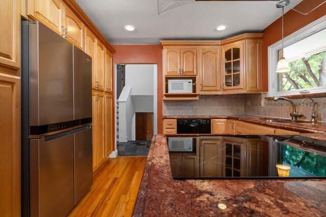 kitchen with a sink, freestanding refrigerator, light wood finished floors, glass insert cabinets, and tasteful backsplash