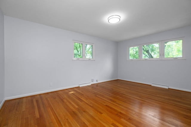 empty room featuring baseboard heating, light wood-style flooring, and baseboards