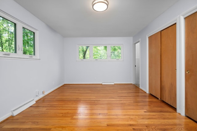 unfurnished bedroom featuring light wood finished floors, a baseboard radiator, two closets, and baseboards