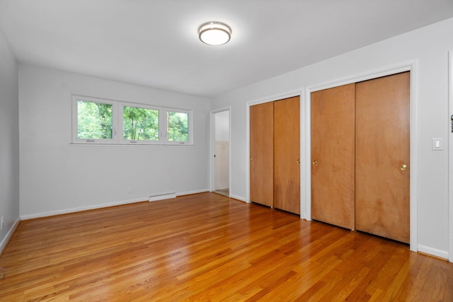 unfurnished bedroom featuring light wood finished floors, two closets, and baseboards