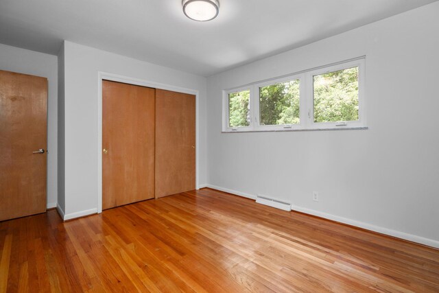 unfurnished bedroom featuring light wood finished floors, baseboards, baseboard heating, and a closet