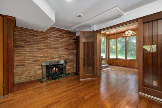 unfurnished living room featuring wooden walls, visible vents, wood finished floors, stairs, and a brick fireplace