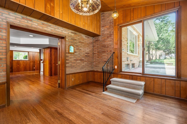 unfurnished room featuring stairs, brick wall, wood walls, and wood finished floors