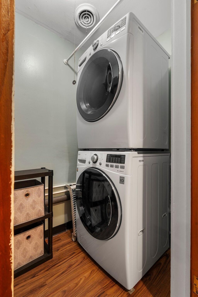 clothes washing area with laundry area, visible vents, stacked washer / dryer, and wood finished floors