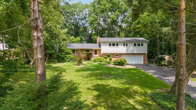 tri-level home featuring aphalt driveway, brick siding, a chimney, an attached garage, and a front lawn