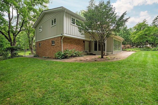 view of property exterior featuring a lawn, fence, a patio area, board and batten siding, and brick siding