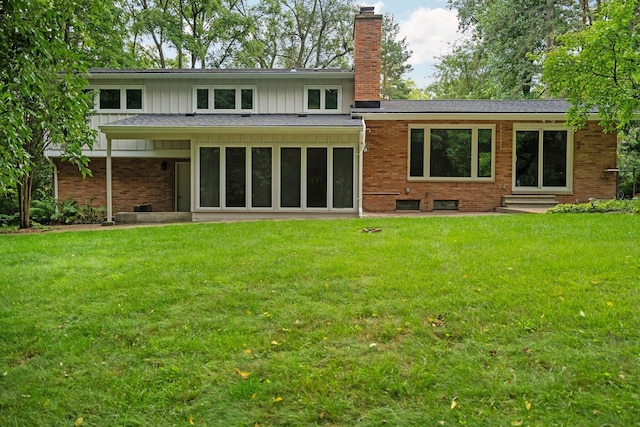 rear view of property featuring a yard, brick siding, board and batten siding, and a chimney