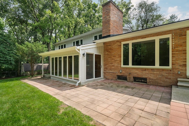 back of house featuring a patio, brick siding, a sunroom, a lawn, and a chimney