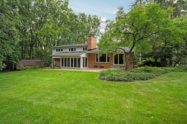 back of property with an outbuilding, brick siding, a yard, a chimney, and a patio area