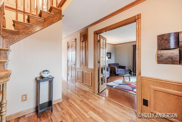 hallway featuring a textured ceiling, light wood-style floors, stairs, wainscoting, and crown molding