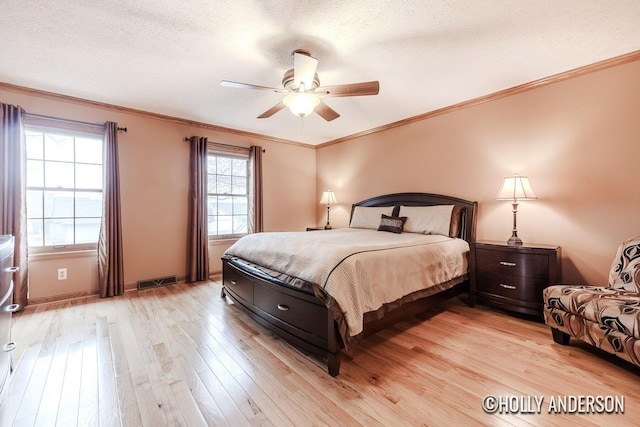 bedroom featuring ornamental molding, light wood finished floors, a textured ceiling, and visible vents