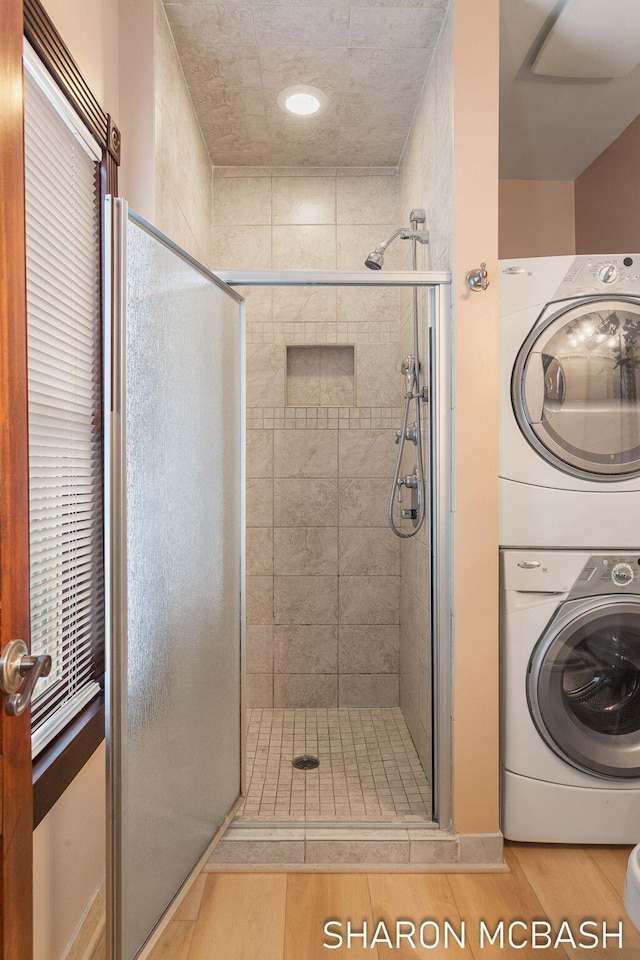 bathroom featuring a shower stall, stacked washer / drying machine, and wood finished floors