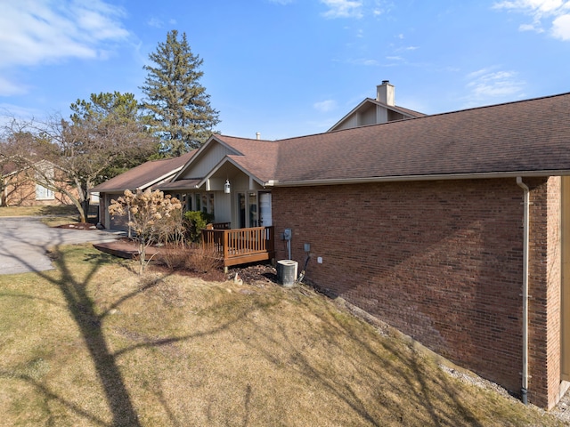 view of front of home with central AC, roof with shingles, a front yard, brick siding, and a chimney