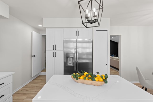 kitchen with white cabinets, stainless steel refrigerator with ice dispenser, pendant lighting, a notable chandelier, and light wood-type flooring