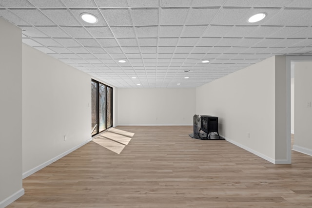 basement with recessed lighting, light wood-type flooring, a wood stove, and baseboards