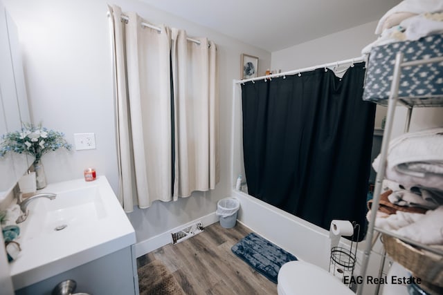 bathroom with toilet, shower / bath combo, vanity, wood finished floors, and baseboards