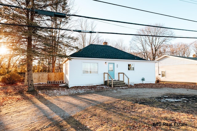 view of front of home featuring a shingled roof, a chimney, and fence