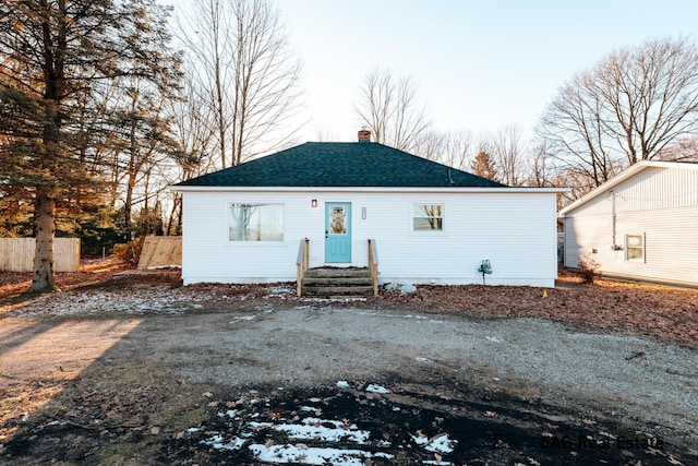 view of front of house with driveway, a shingled roof, a chimney, and fence