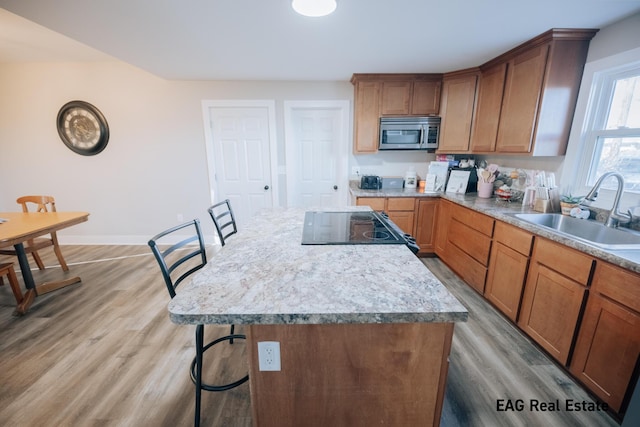 kitchen with a breakfast bar area, stainless steel microwave, a sink, light wood-type flooring, and range with electric cooktop