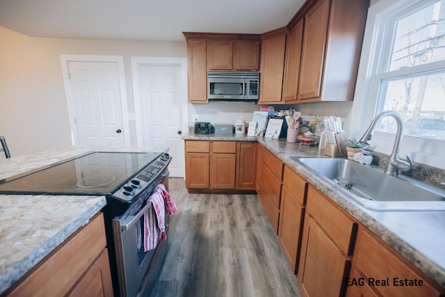 kitchen featuring brown cabinetry, stainless steel appliances, a sink, and light wood finished floors