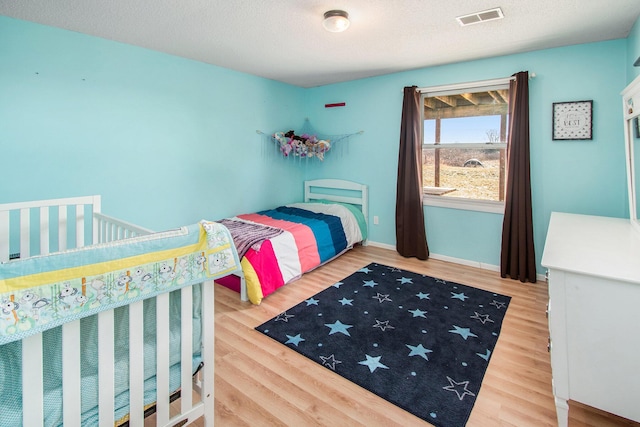 bedroom with a textured ceiling, wood finished floors, visible vents, and baseboards