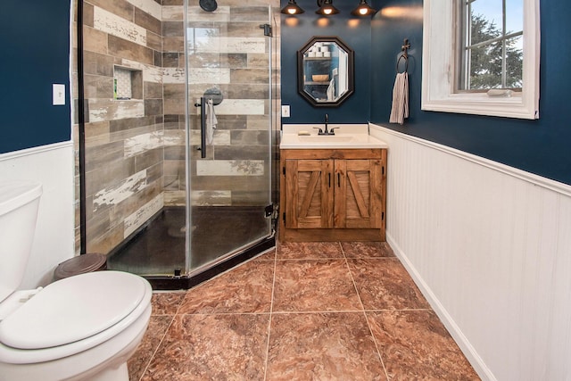 full bath featuring vanity, wainscoting, a shower stall, and toilet