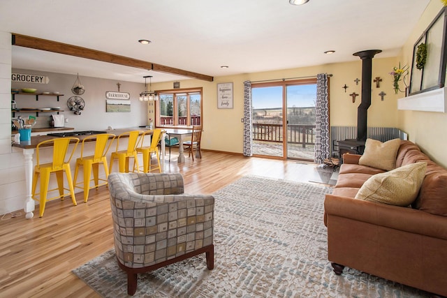 living room with a wood stove, beamed ceiling, baseboards, and wood finished floors