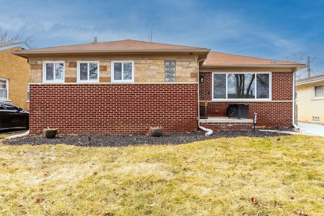 rear view of house featuring a yard, brick siding, and stone siding