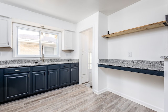 kitchen with light wood finished floors, baseboards, white cabinetry, blue cabinets, and a sink