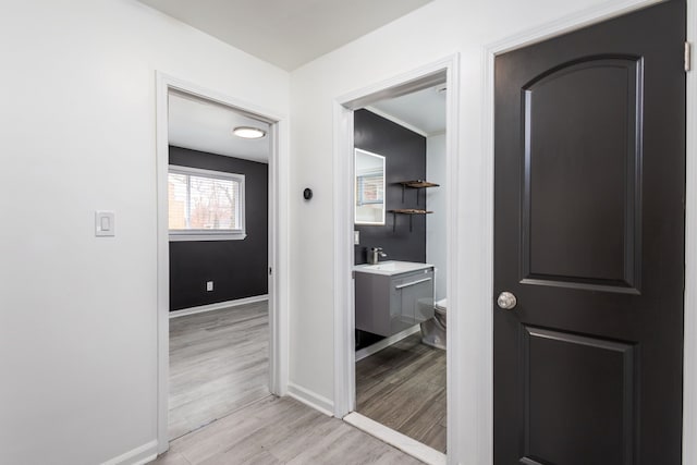 hallway featuring a sink, light wood-type flooring, and baseboards