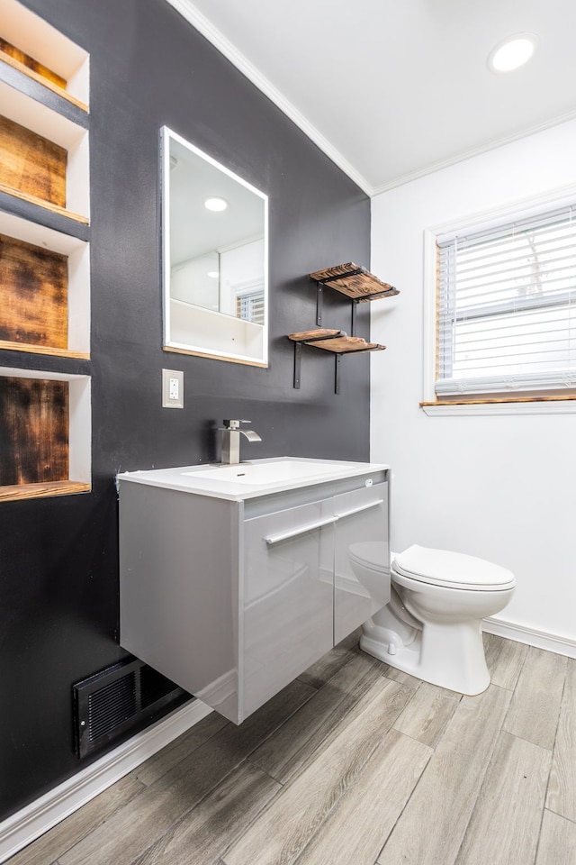 bathroom with visible vents, toilet, ornamental molding, wood finished floors, and vanity