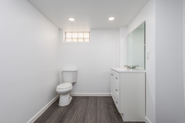 half bath featuring toilet, wood finished floors, recessed lighting, baseboards, and vanity