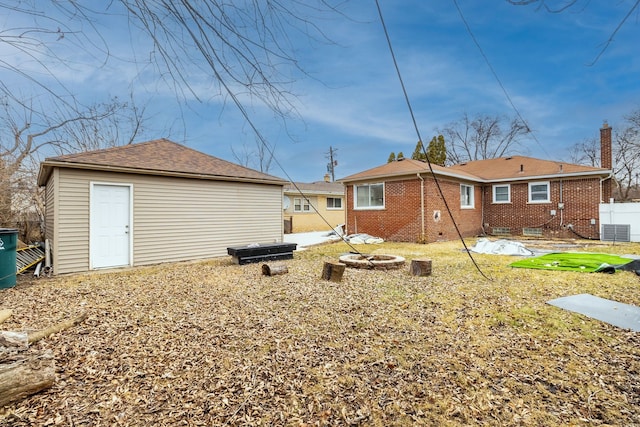 back of house featuring an outbuilding, central AC unit, fence, an outdoor fire pit, and brick siding