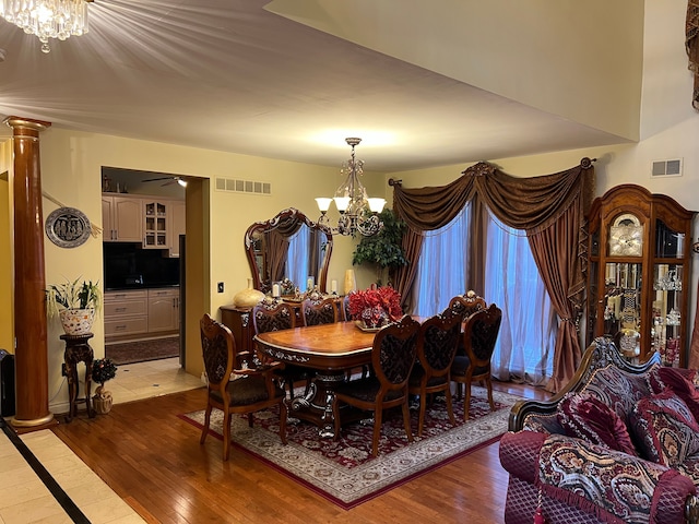 dining space featuring ornate columns, light wood-type flooring, visible vents, and a notable chandelier