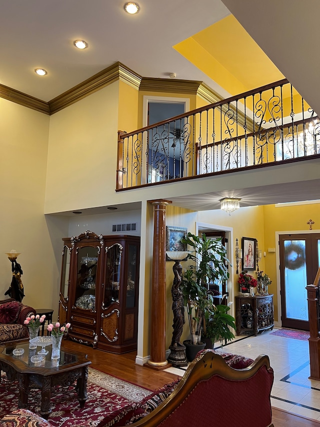 living room with a towering ceiling, ornate columns, visible vents, and crown molding