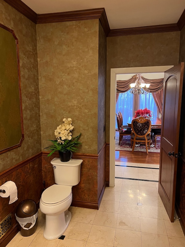 bathroom with toilet, an inviting chandelier, ornamental molding, and wainscoting