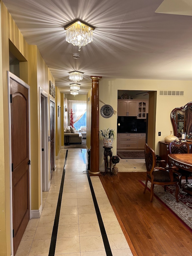 hallway with visible vents, baseboards, light wood-type flooring, an inviting chandelier, and ornate columns